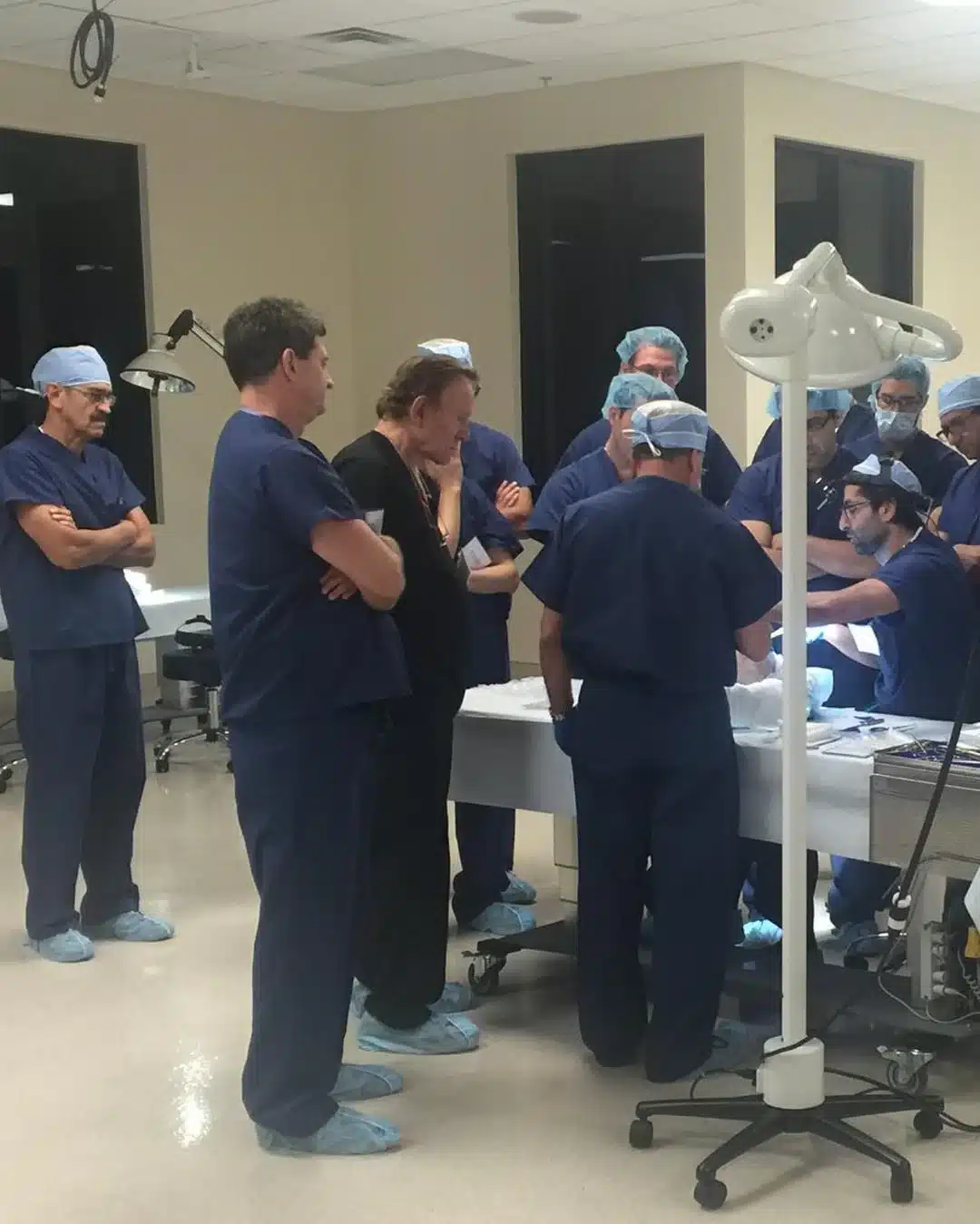 Dr. Robert J. Troell, MD, FACS with practicing surgeons in scrubs gathered around a training table at the Implantech hands-on implant cadaver course