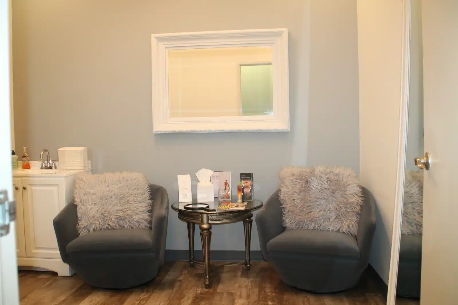 Consultation room at Troell Cosmetic Surgery on South Fort Apache Road, Las Vegas &mdash; two grey armchairs, a glass side table, and a framed mirror
