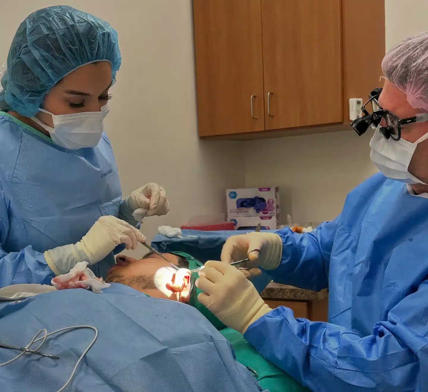 Dr. Robert J. Troell, in surgical loupes, and a surgical assistant operating on a draped patient's ear during an otoplasty at Troell Cosmetic Surgery in Las Vegas